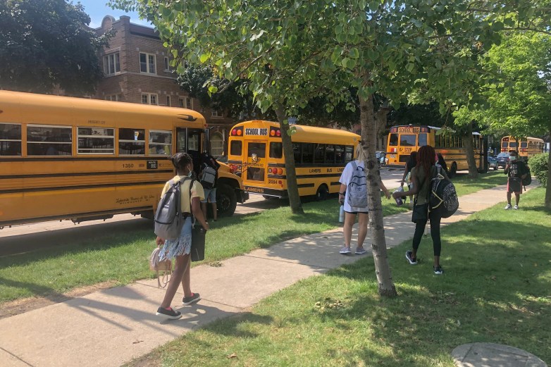 Students walk near yellow school buses.