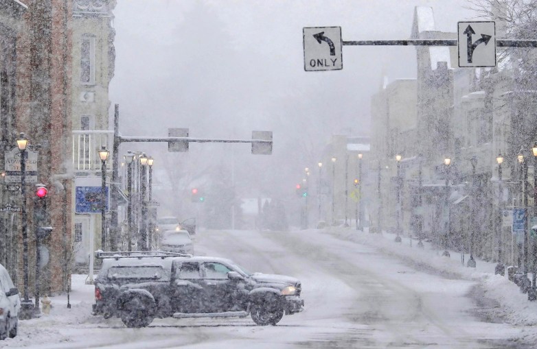 A truck crosses a street as snow falls during a winter storm.