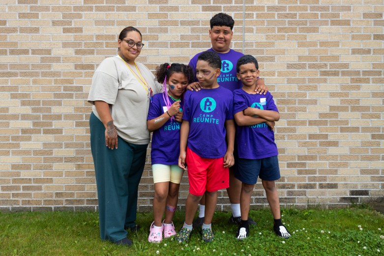 Woman poses with four children in front of brick wall.