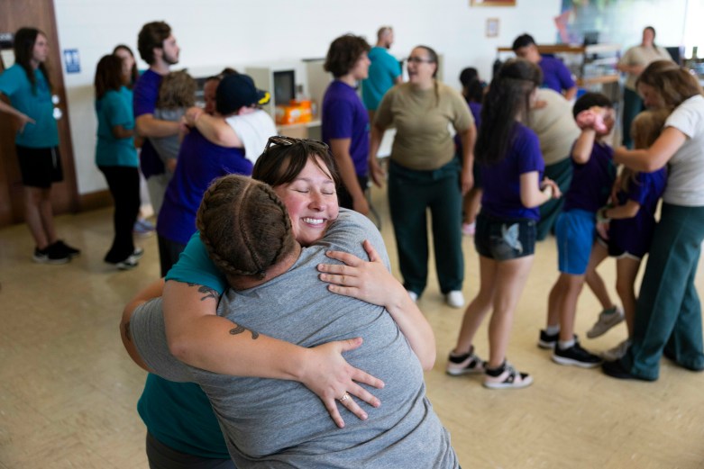Smiling woman hugs another person with others in the background.