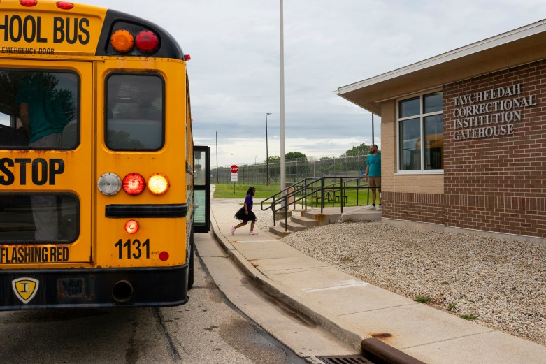 Child wearing dress walks from yellow school bus to Taycheedah Correctional Institution Gatehouse building.
