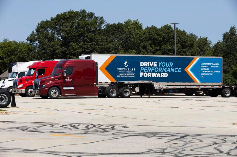 Three semi-trucks are parked in a lot, including a trailer with text reading 
