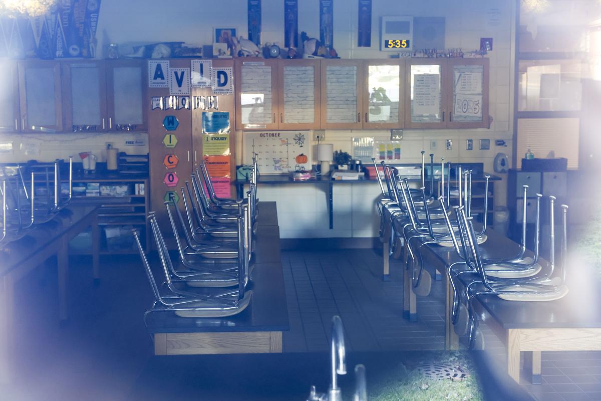 An empty classroom with chairs stacked upside down on tables, colorful posters on cabinets and a clock showing 5:35.