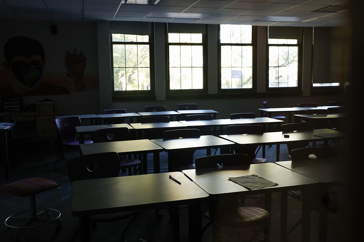 An empty classroom with rows of desks and chairs and sunlight streaming through windows.