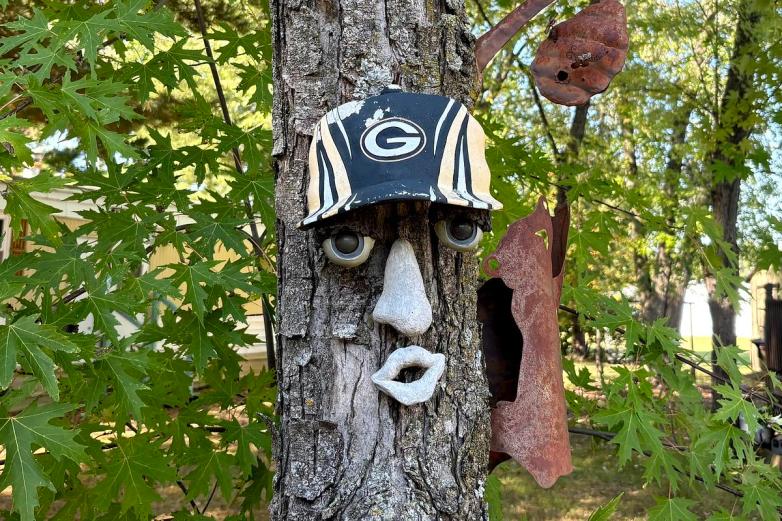A tree trunk decorated with a face made of sculpted eyes, nose and mouth with a cap with a 