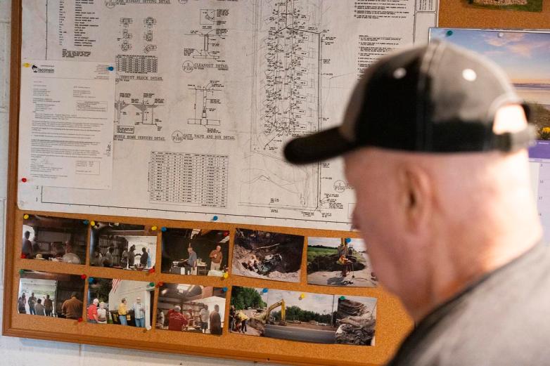 A person wearing a cap looks at a bulletin board covered with diagrams and photos.