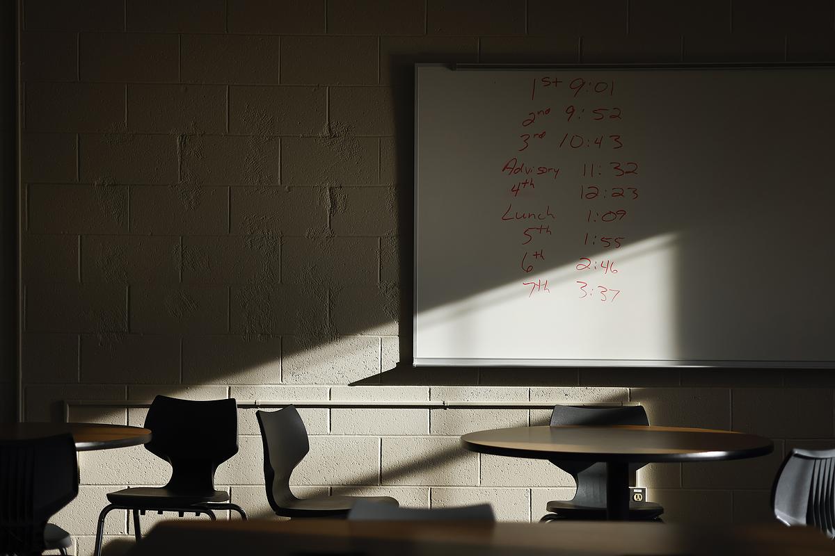 Sunlight falls across a whiteboard with red numbers and words and empty chairs and tables.