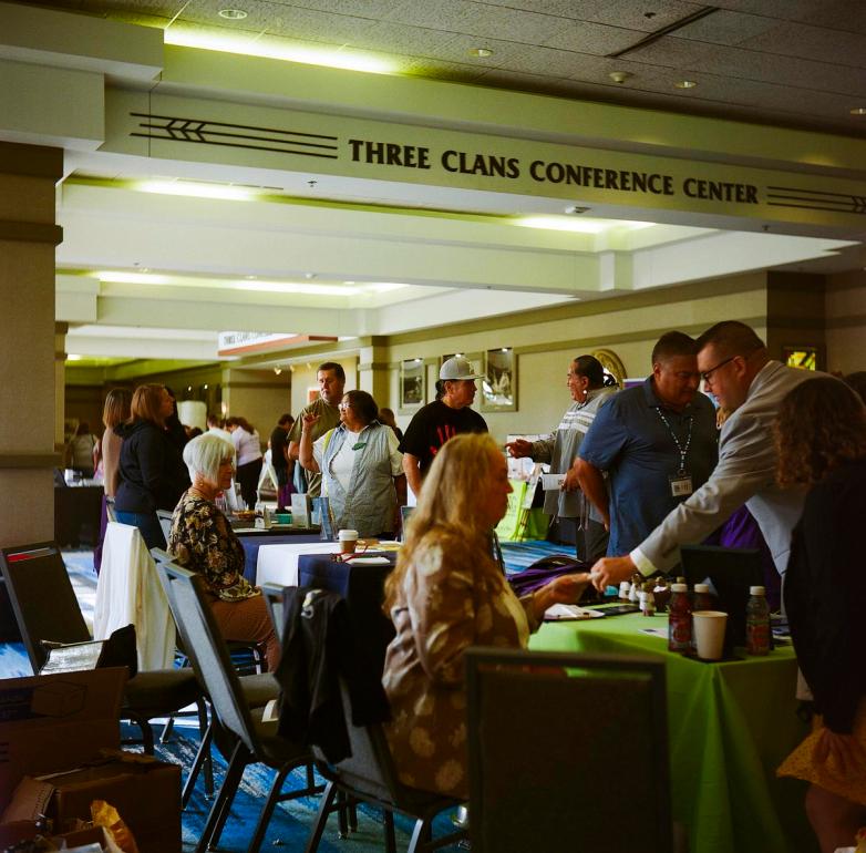 People stand and sit at tables in a hallway under a sign reading 