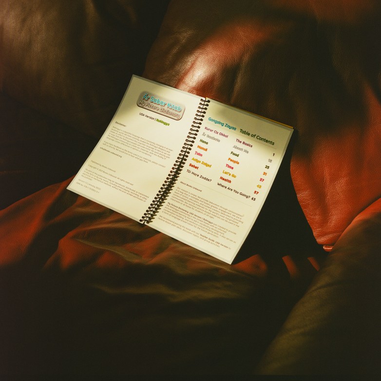 An open spiral-bound booklet rests on leather furniture, showing a table of contents and text pages illuminated by sunlight.