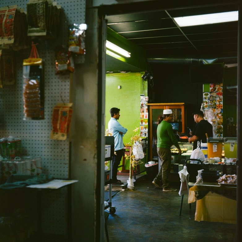 People stand in a room with drinks, packaged items and a display case visible under fluorescent lighting.