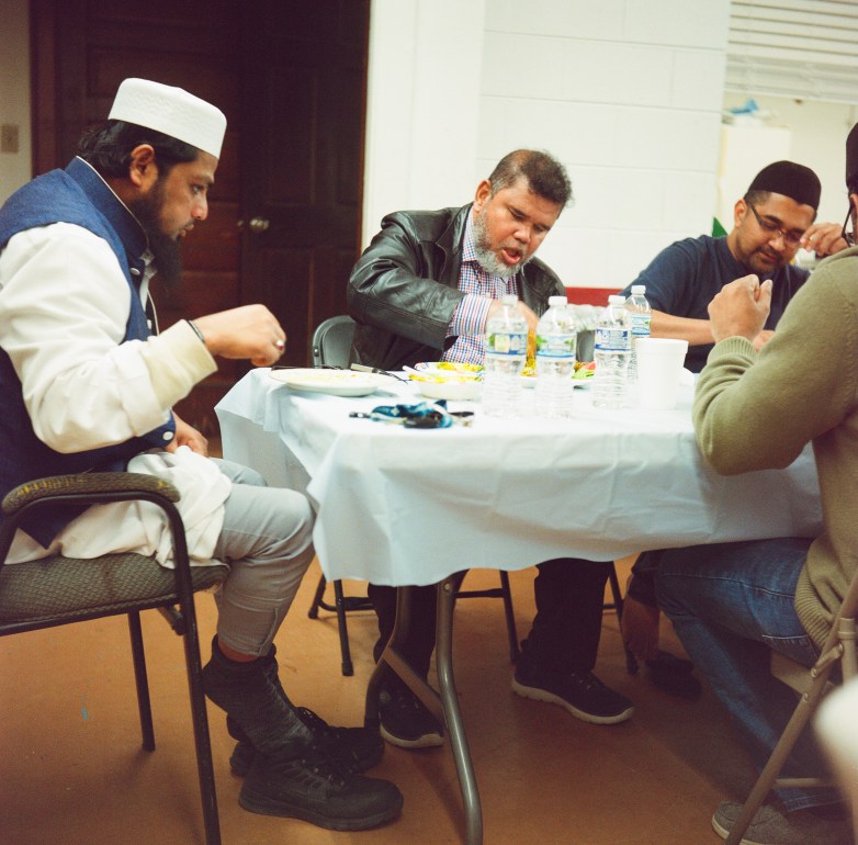 People sit around a table covered with plates of food and water bottles.