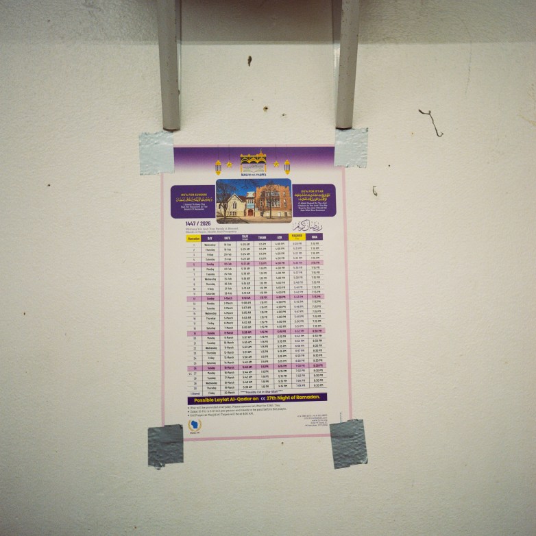 A printed schedule labeled for Ramadan is taped to a wall with visible strips of tape holding it in place.