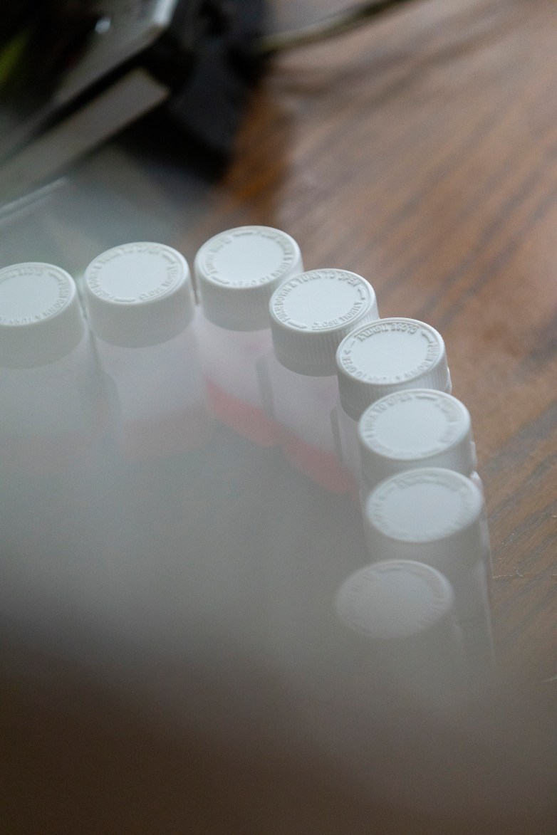 Small bottles with white caps are arranged in a semicircle on a wooden surface, with red liquid visible inside some of the bottles.