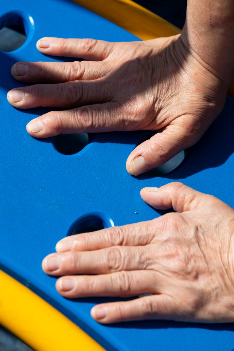 Two hands rest on a blue surface with round holes, with yellow bars visible at the edges.