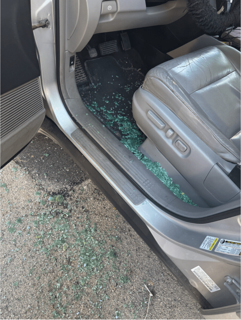 Green glass is shattered inside a car and on the ground.