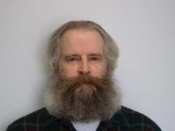 A portrait shows a person with long hair and a full beard facing the camera against a plain light background.