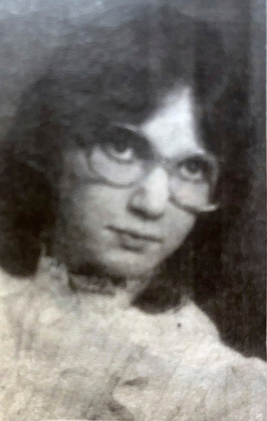 A black-and-white portrait shows a person with shoulder-length hair and glasses looking toward the camera.