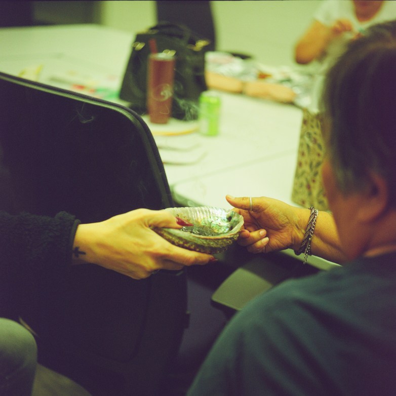 One person passes a shell to another person seated at a table, while others sit nearby.