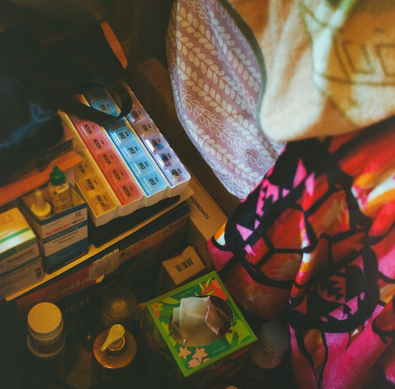 Labeled pill organizers, medicine bottles, tissues and other personal care items are seen next to blankets.