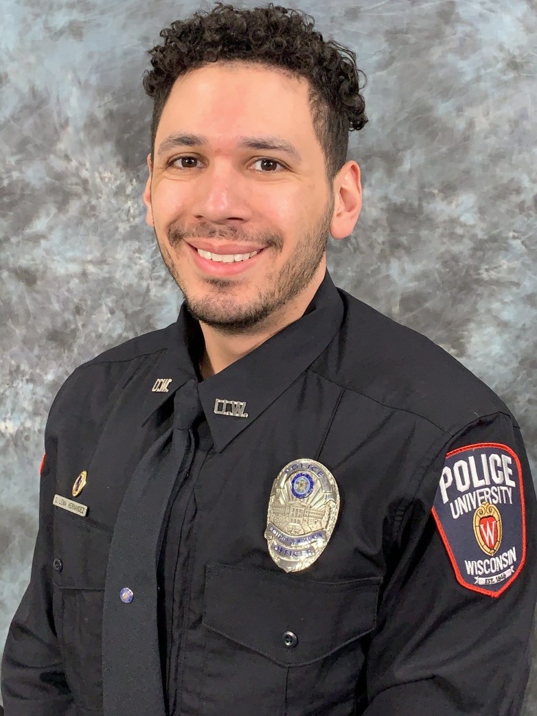 A person wears a black uniform with a badge and a shoulder patch reading 