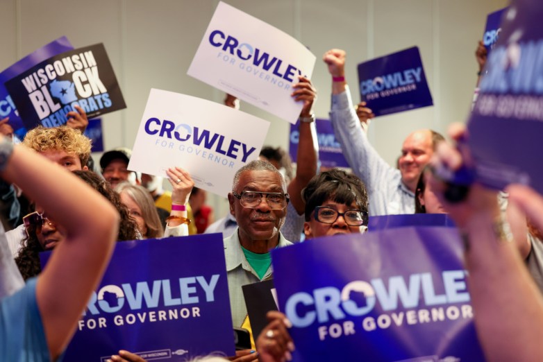 People hold purple and white signs reading 