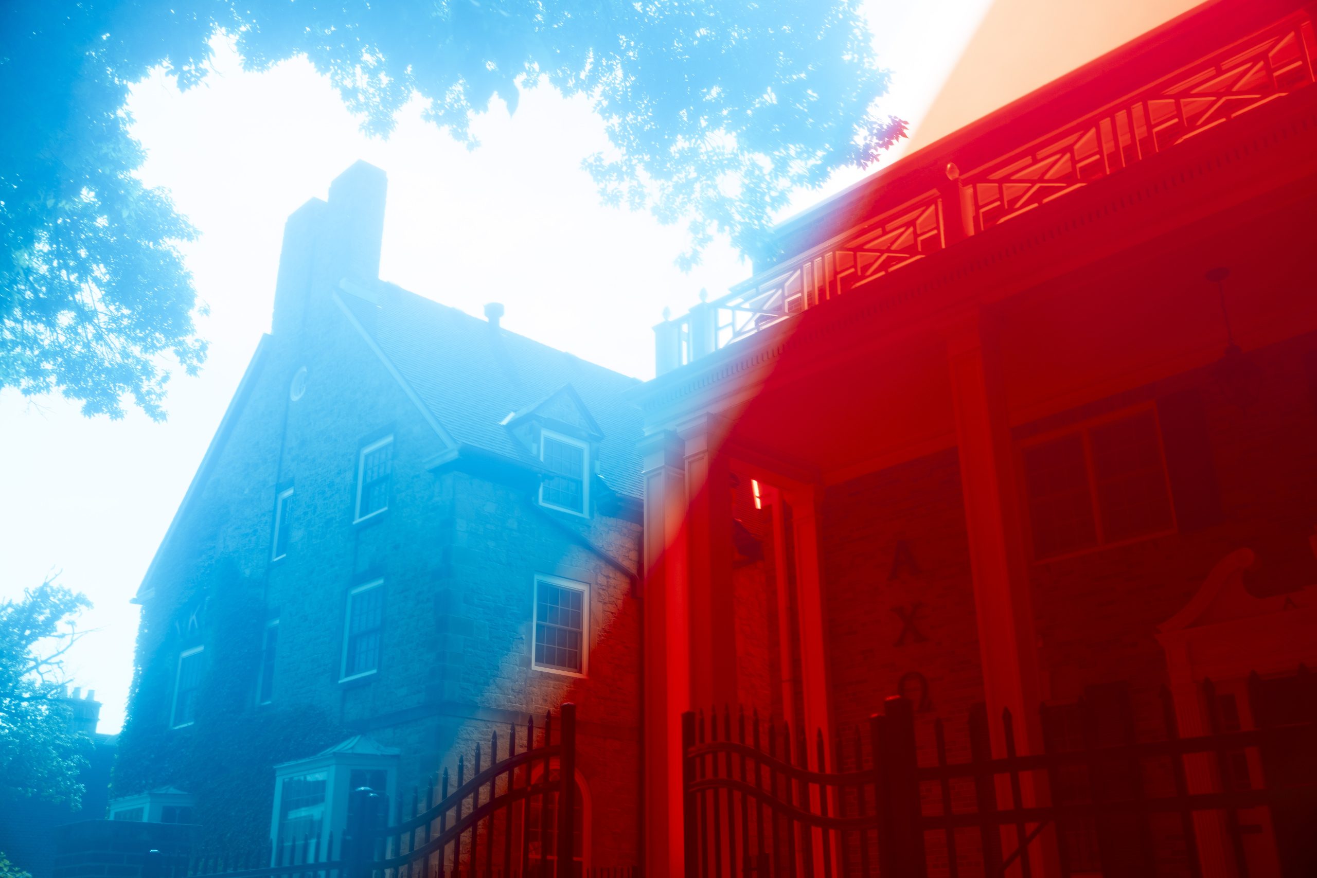 A stone building and covered entrance are washed in blue and red light, with trees and a metal fence nearby.