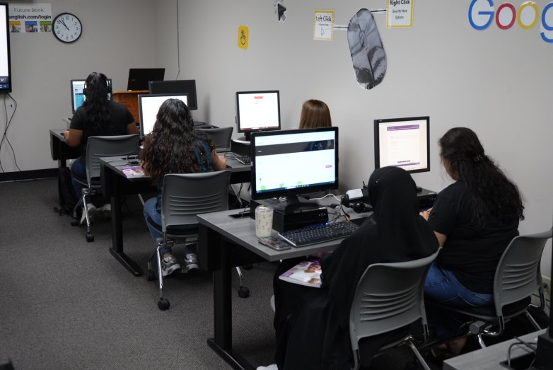 People sit at desktop computers in a room with signs explaining mouse clicks and a web login address on the walls.