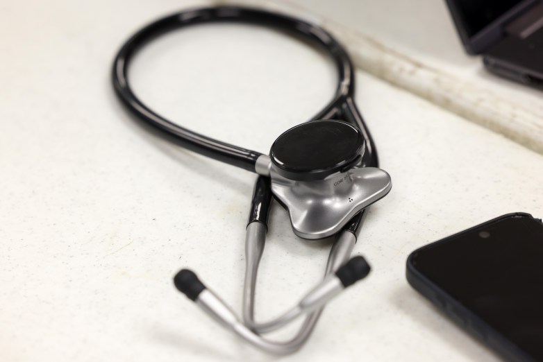 A black and silver stethoscope rests on a white surface beside part of a black rectangular object.