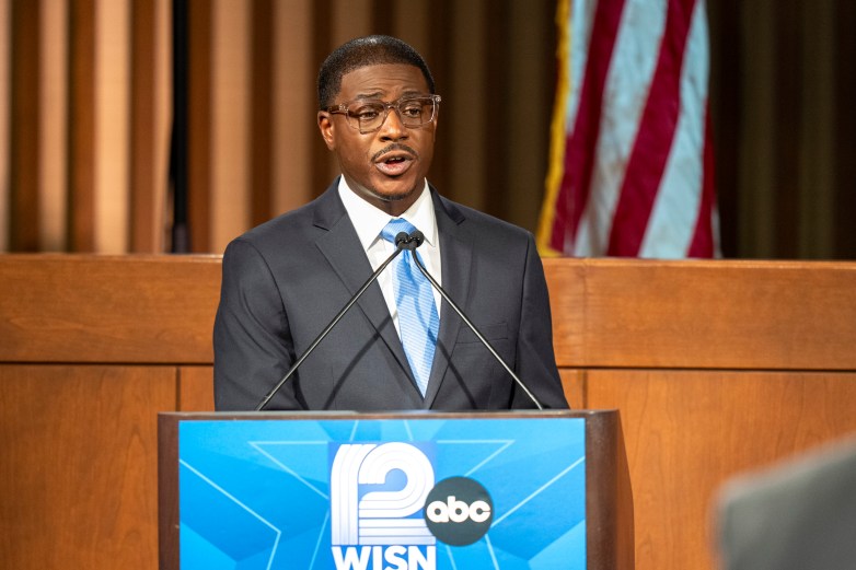 A man in a suit speaks at a podium that says 12 WISN ABC